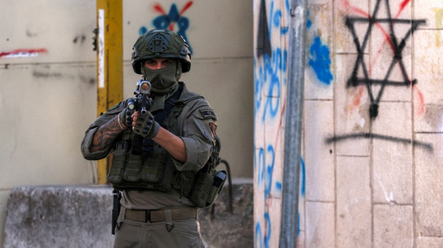 Un soldat israélien monte la garde alors que des colons israéliens visitent le centre de la vieille ville et le marché de la ville palestinienne d'Hébron, en Palestine occupée, le 28 juin 2025.