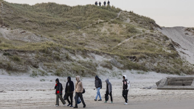 Des gendarmes français observent la plage alors que des migrants marchent pour monter à bord d'un bateau de passeurs qui tentent de traverser la Manche au large de la plage d'Equihen, dans le nord de la France, le 30 juin 2025.