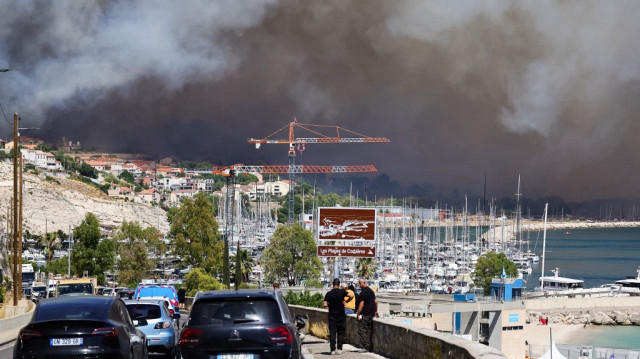 Des gens regardent près de la plage des Corbières, à Marseille, dans le sud de la France, le 8 juillet 2025, alors que la fumée d'un feu de forêt fait rage à l'arrière-plan.