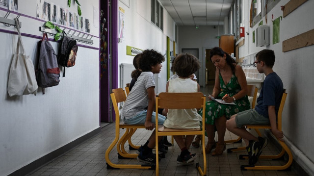 Un petit groupe d'enfants assiste à un cours à l'extérieur de leur salle de classe pour trouver de l'air frais dans le couloir d'une école élémentaire pendant une vague de chaleur à Bordeaux, dans le sud-ouest de la France, le 1er juillet 2025.