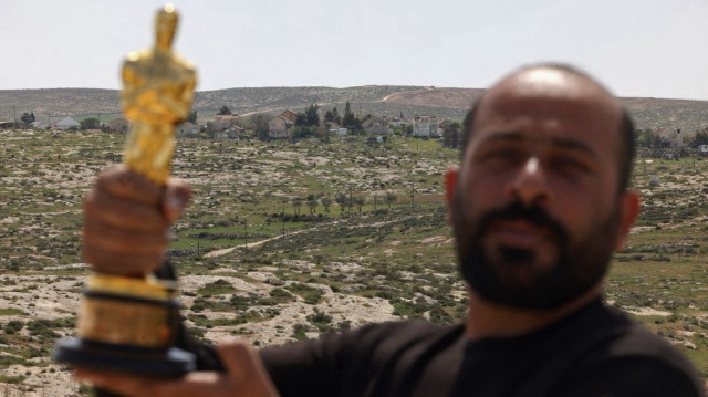 Le cinéaste palestinien Hamdan Ballal, lauréat d'un Oscar pour le documentaire « No Other Land », pose pour une photo avec son Oscar, avec en arrière-plan une colonie israélienne, alors qu'il se remet d'une attaque perpétrée par des colons israéliens à son domicile, dans son village de Susya, au sud de la Palestine occupée, le 26 mars 2025.