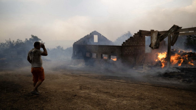 Un habitant passe devant une ferme incendiée par les feux de forêt dans le village de Lubizhde, le 26 juillet 2025, alors que les températures atteignaient 40 degrés Celsius au Kosovo.