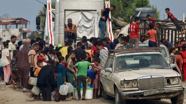 Des Palestiniens font la queue pour s'approvisionner en eau sous une chaleur étouffante dans le quartier de Mawasi, à Khan Yunis, dans le sud de la bande de Gaza, le 12 août 2025.