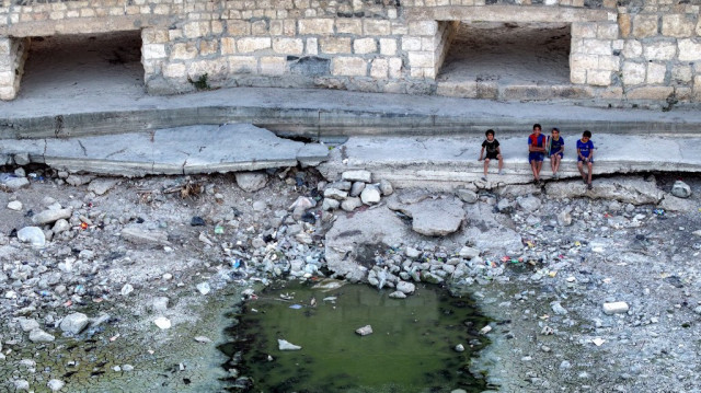 Cette vue aérienne montre des enfants assis près du lit désormais asséché de l'Oronte (Assi) en Syrie, lors d'une sécheresse extrême dans la ville de Jisr al-Shughur, dans la province d'Idlib, au nord-ouest de la Syrie, le 4 août 2025.