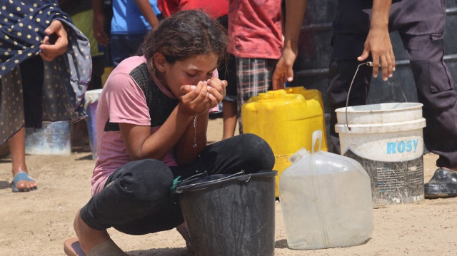 Une fillette boit de l'eau dans un seau en plastique tandis que des Palestiniens déplacés collectent de l'eau dans la région de Mawasi, près de Khan Yunis, le 14 août 2025.