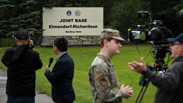 Des journalistes travaillent près d'une entrée de la base militaire commune Elmendorf-Richardson à Anchorage, en Alaska, le 14 août 2025, à la veille de la rencontre prévue le 15 août entre le président américain Donald Trump et le président russe Vladimir Poutine.