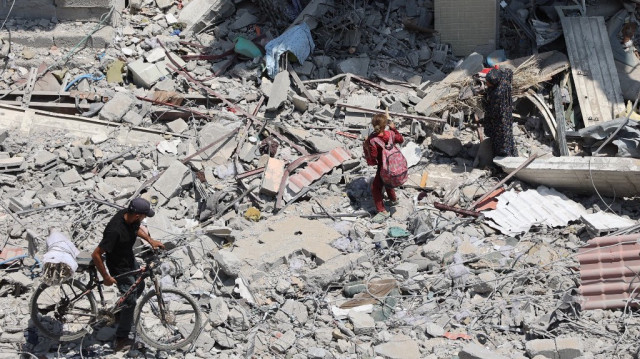 Des Palestiniens marchent sur des décombres et des débris dans le quartier d'al-Tuffah, à Gaza, le 14 août 2025.