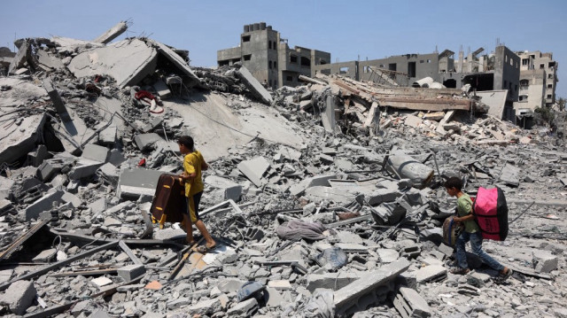 Des garçons palestiniens traversent des décombres en portant des sacs dans le quartier d'al-Tuffah à Gaza, le 14 août 2025.