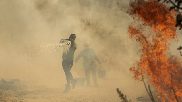 Des habitants utilisent des seaux d'eau pour éteindre un incendie qui menace leur maison dans le village portugais d'Antas, à Trancoso, le 15 août 2025. Les incendies qui font rage à travers le Portugal ont fait leur première victime aujourd'hui, lorsque l'ancien maire de la ville orientale de Guardadied a succombé à ses blessures, a annoncé le président Marcelo Rebelo de Sousa.