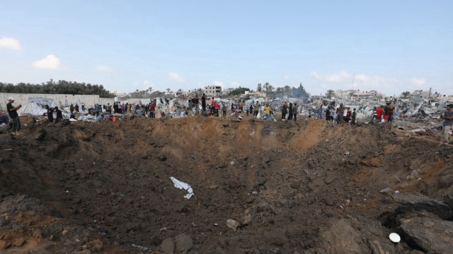 Des Palestiniens déplacés se rassemblent autour d'un cratère d'impact, laissé par une frappe israélienne, dans un camp pour personnes déplacées à Deir el-Balah, dans le centre de la bande de Gaza, le 21 août 2025.