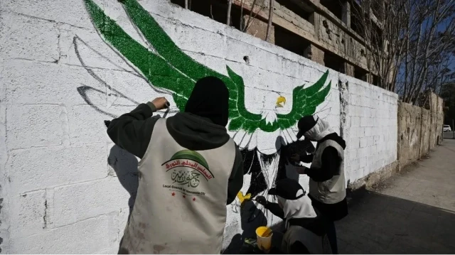 Des femmes peignent une fresque murale à Hammuriyeh, dans l'ancienne région rebelle de la Ghouta orientale, à la périphérie de Damas, le 14 janvier 2025, alors que les Syriens déplacés par la guerre et vivant dans le nord-ouest de la Syrie, contrôlé par l'opposition, retournent dans leurs maisons après la destitution du président Bachar al-Assad.