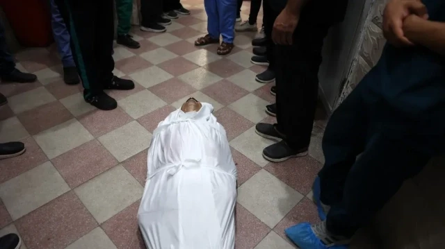 Des collègues entourent le corps recouvert d'un linceul d'Ahmad Qandil, un médecin palestinien tué lors d'une frappe israélienne, alors que son corps gît sur le sol de l'hôpital Maamadani (baptiste) de la ville de Gaza, le 13 juillet 2025.