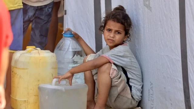 Une fillette est assise près de réservoirs d'eau tandis que des Palestiniens déplacés attendent pour aller chercher de l'eau dans la région de Mawasi, à Khan Yunis, le 14 août 2025. Les organisations internationales s'efforcent de fournir de l'eau potable à la population alors que la crise s'aggrave et que les maladies se propagent en raison du manque d'hygiène dans la bande de Gaza.
