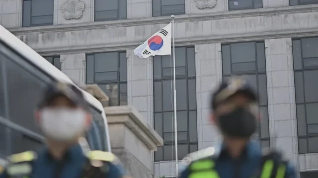 Un drapeau sud-coréen flotte au vent tandis que des policiers se tiennent sur une route à Séoul, le 1er avril 2025, devant la Cour constitutionnelle, qui rendra son verdict tant attendu sur la destitution du président Yoon Suk Yeol le 4 avril, plusieurs mois après sa suspension pour avoir déclaré la loi martiale.