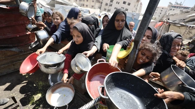 Gazaouis attedant sous une chaleur accablante pour obtenir une casserole de nourriture, à Gaza, le 24 août 2025.