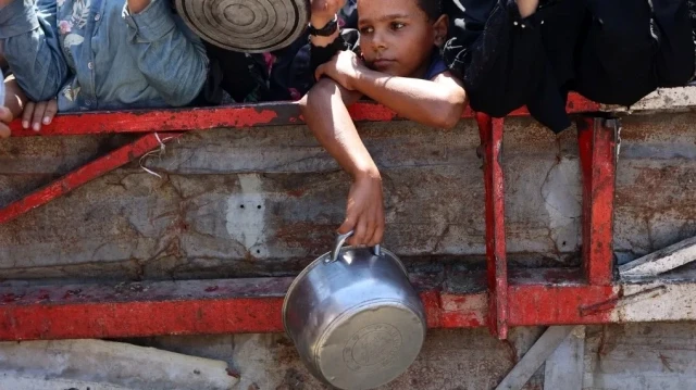 Un garçon palestinien tient un pot vide alors qu'il attend avec d'autres personnes pour recevoir du riz cuit devant une cuisine caritative à Gaza City, le 23 août 2025.