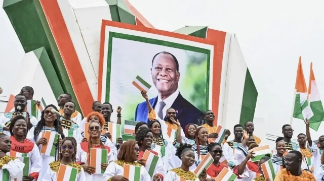 Des partisans se tiennent à côté d'une photo du président ivoirien Alassane Ouattara lors d'un défilé militaire marquant le 65e anniversaire de l'indépendance de la Côte d'Ivoire à Bouaké, le 7 août 2025.