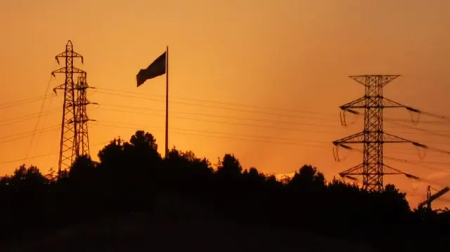 Le soleil se couche derrière des pylônes électriques à haute tension dans l'ouest de Téhéran, le 11 août 2025.