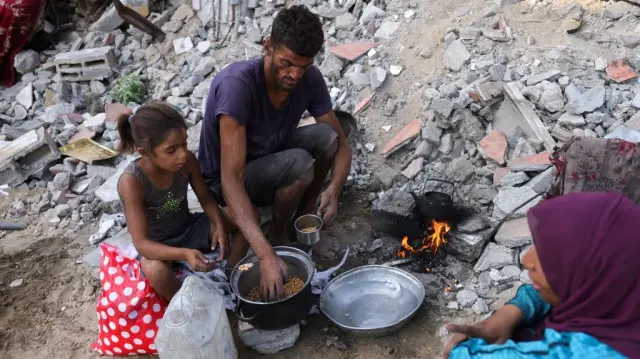 Un Palestinien déplacé et sa famille réchauffent des pois chiches alors qu'ils sont assis au milieu des décombres du quartier de Saftawi, à l'ouest de Jabalia, dans le nord de la bande de Gaza, le 24 août 2025, alors que la guerre entre Israël et le groupe militant palestinien Hamas se poursuit.