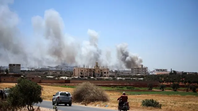 Des personnes circulent sur une route alors qu'un panache de fumée s'élève à la suite d'une explosion à Maarrat Misrin, dans le nord de la province d'Idlib, en Syrie, le 24 juillet 2025.