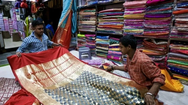 Un vendeur de vêtements (à gauche) présente un sari traditionnel en soie de Banarasi à une cliente dans une boutique de vêtements à Varanasi, le 24 août 2025.