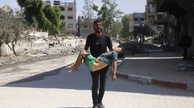 Un homme porte le corps d'un garçon palestinien, tué alors qu'il fuyait son domicile, dans le quartier de Saftawy à Jabalia, le 26 août 2025.