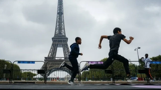 Deux enfants participent à une activité de course à pied au Champ-de-Mars, avec la tour Eiffel en arrière-plan, à Paris, le 20 août 2025, dans le cadre de la 46e édition d'une journée d'activités pour les enfants qui ne partent pas en vacances, organisée par l'ONG française Secours Populaire.