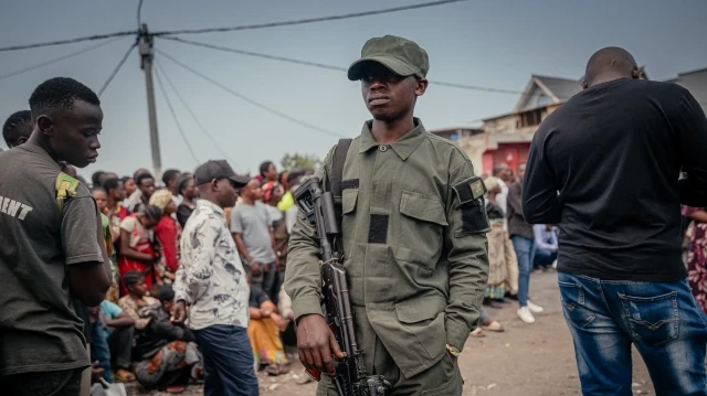 Un soldat de l'AFC/M23 monte la garde avec un fusil Kalachnikov devant la foule rassemblée, assurant la sécurité du maire de la ville et de sa délégation à Goma, le 24 juillet 2025. Ce rassemblement s'inscrit dans le cadre d'une stratégie de sensibilisation visant à instaurer la confiance auprès de la population locale.