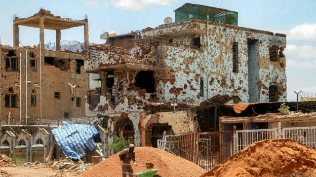 Un ouvrier pellette des cailloux d'un tas dans une brouette près d'un bâtiment fortement endommagé sur un chantier dans la banlieue de Lamab, à la périphérie sud-ouest de Khartoum, la capitale du Soudan, le 30 juillet 2025, alors que les habitants reviennent dans le cadre des efforts de reconstruction.