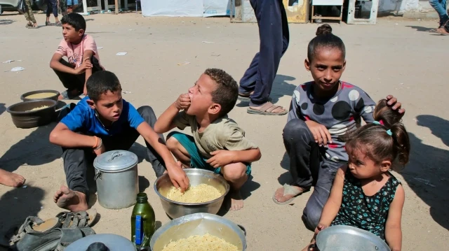 Des enfants palestiniens mangent du riz cuit après avoir réussi à obtenir des portions de nourriture chaude dans une cuisine caritative à Khan Yunis, dans le sud de la bande de Gaza, le 27 août 2025.