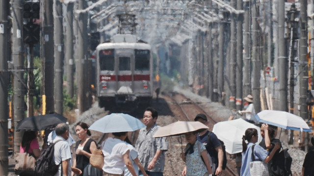 Une brume de chaleur est visible à l'arrière-plan tandis que des piétons munis de parapluies traversent une voie ferrée par une journée chaude à Tokyo, le 5 août 2025.