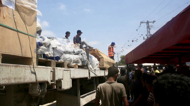 Un camion transportant des pièces pour l'installation d'une conduite d'eau passe devant des personnes du côté palestinien de Rafah, le 28 juillet 2025.