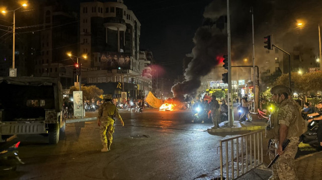 Des soldats libanais regardent des partisans du Hezbollah bloquer les rues avec des pneus enflammés alors qu'ils se rassemblent en voitures et en motos pour protester contre l'approbation par le gouvernement d'un plan de désarmement, dans la banlieue sud de Beyrouth, le 8 août 2025.
