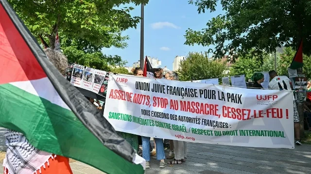Des manifestants se tiennent à côté d'une banderole sur laquelle on peut lire « Union juive pour la paix (UJFP) - assez de paroles, arrêtez le massacre, cessez-le-feu ! Nous exigeons des autorités françaises des sanctions immédiates contre Israël et le respect du droit international » lors d'un rassemblement pro-palestinien intitulé "Stop au génocide" place de la Bastille à Paris, le 9 août 2025.
