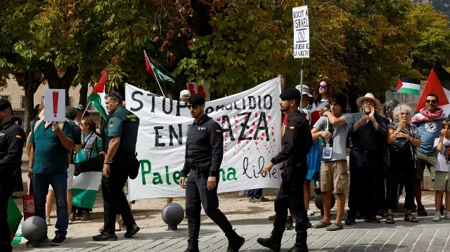 Des agents de la Guardia Civil marchent tandis que des manifestants pro-palestiniens brandissent une banderole sur laquelle on peut lire "Stop au génocide à Gaza, libérez la Palestine" lors de la 20e étape de la Vuelta a Espana 2025, une course de 156 km entre Robledo de Chavela et Bola del Mundo, à El Escorial, le 13 septembre 2025.