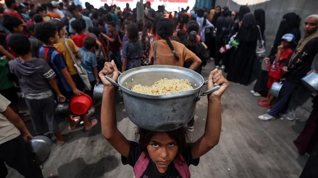 Un enfant palestinien s'éloigne avec un pot de riz obtenu dans une cuisine communautaire du camp de réfugiés de Nuseirat, dans le centre de la bande de Gaza, le 14 septembre 2025, alors que l'ONU a déclaré une famine après près de deux ans de guerre.
