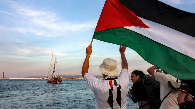 Un homme agite un drapeau palestinien à l'intention d'autres militants et défenseurs des droits humains à bord d'un navire quittant le port de Bizerte, dans le nord de la Tunisie, le 14 septembre 2025, pour rejoindre les derniers bateaux participant à la flottille mondiale Sumud, à destination de la bande de Gaza afin de briser le blocus israélien sur le territoire palestinien.