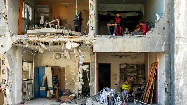Un homme et des enfants sont assis dans des pièces exposées au vent dans un bâtiment fortement endommagé près de la Tour du Soldat inconnu, détruite par les bombardements israéliens pendant la nuit, dans le quartier de Rimal à Gaza, le 15 septembre 2025.