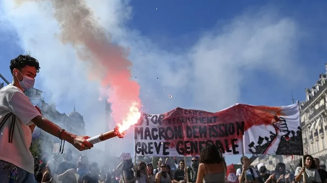 Un manifestant allume une fusée éclairante tandis qu'une banderole sur laquelle on peut lire "Stop à l'austérité, au réarmement, démission de Macron, grève générale" est brandie à Montpellier, dans le sud de la France, le 18 septembre 2025, lors d'une journée de grèves et de manifestations nationales organisées par les syndicats pour protester contre le budget national français.