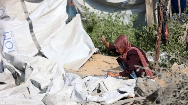 Une femme palestinienne déplacée répare une tente déchirée, après une frappe israélienne nocturne qui a rasé un bâtiment et endommagé les abris temporaires environnants, dans le quartier de Rimal à Gaza, le 13 septembre 2025.