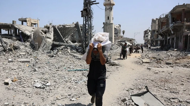Un Palestinien passe devant des bâtiments détruits en transportant des objets récupérés dans le quartier d'al-Tuffah à Gaza, le 14 août 2025.