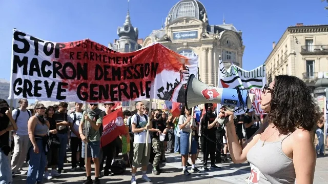Un manifestant crie dans un mégaphone tandis qu'une banderole portant l'inscription "Stop à l'austérité, au réarmement, démission de Macron, grève générale" est brandie à Montpellier, dans le sud de la France, le 18 septembre 2025, lors d'une journée de grèves et de manifestations nationales organisées par les syndicats au sujet du budget national français.