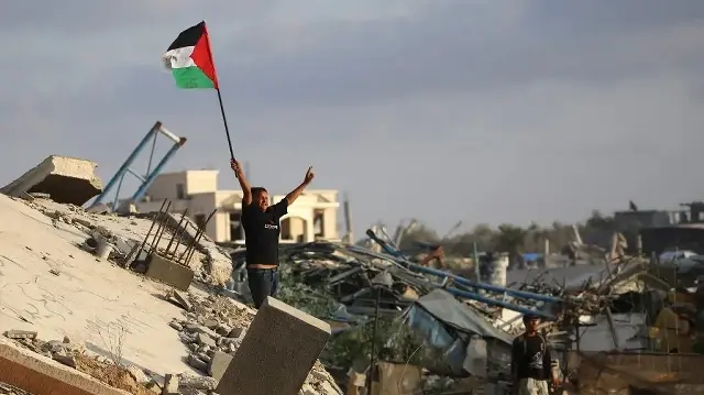 Un enfant palestinien déplacé agite un drapeau national palestinien alors qu’il se tient sur les décombres d’un bâtiment détruit dans le camp de réfugiés de Bureij, dans le centre de la bande de Gaza, le 22 septembre 2025.