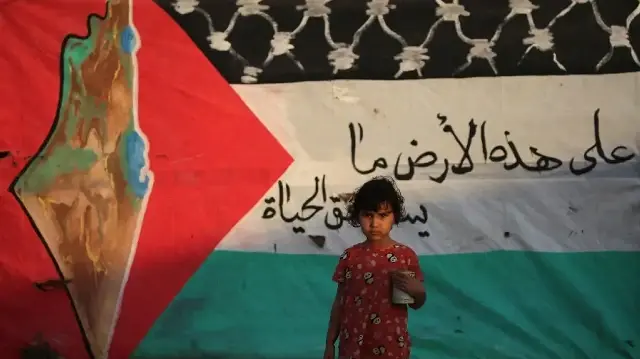 Un enfant palestinien déplacé pose devant un drapeau palestinien dans le camp de réfugiés de Bureij, au centre de la bande de Gaza, le 22 septembre 2025.