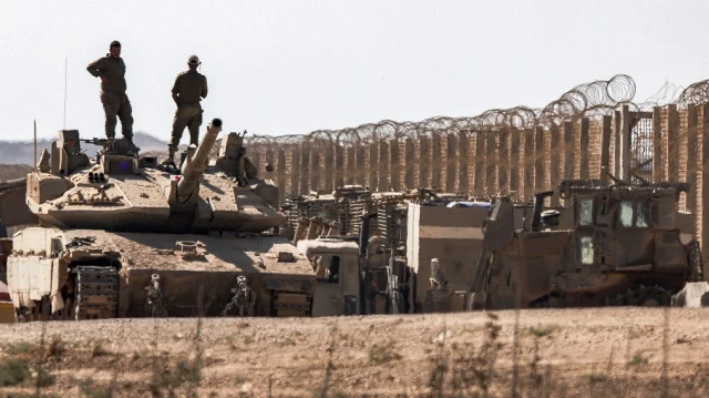 Des soldats de l'armée israélienne se tiennent au sommet de la tourelle d'un char de combat principal Merkava positionné près de bulldozers militaires blindés le long de la frontière avec la bande de Gaza, dans le sud d'Israël, le 2 septembre 2025.