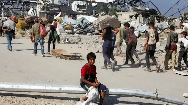 Un garçon est assis sur un lampadaire renversé tandis qu'autour de lui, des gens marchent avec des colis d'aide humanitaire qu'ils ont reçus d'un centre de distribution géré par la Gaza Humanitarian Foundation (GHF), soutenue par les États-Unis et Israël, dans le "couloir de Netzarim", à Nuseirat, dans le centre de la bande de Gaza, le 30 septembre 2025.