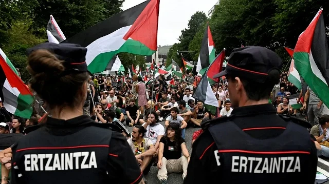 Des manifestants pro-palestiniens brandissant des drapeaux palestiniens et basques manifestent à côté d'officiers de la police régionale basque "Ertzaintza", après la 11e étape de la course cycliste Vuelta, à Bilbao, le 3 septembre 2025.