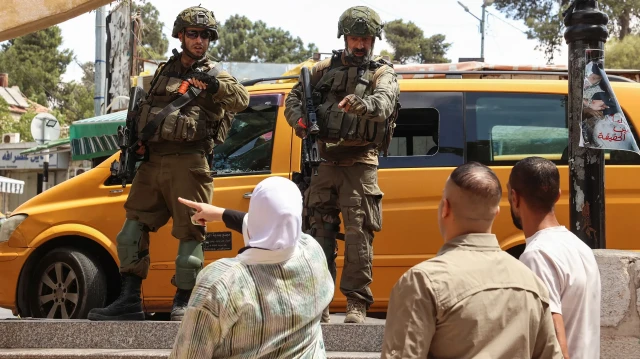 Des Palestiniens discutent avec des soldats israéliens afin d'évacuer une femme âgée qui a souffert d'étouffement à cause des gaz lacrymogènes tirés lors d'un raid sur la ville de Ramallah, en Cisjordanie occupée, le 26 août 2025.