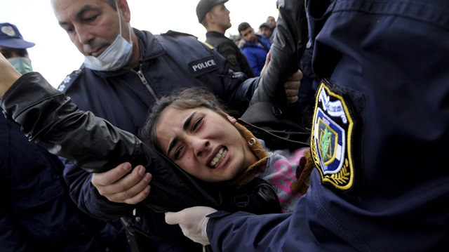 Greek policemen carry away a woman as Syrian, Iraqi and Afghan refugees who try to force their way through the Greek-Macedonian borders are pushed back by Greek police