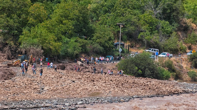 People walk along a damage road after a flood near Santiago, Chile
